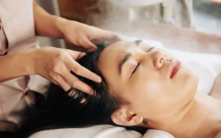 Kỹ thuật viên mát xa da đầu cho khách nữ đang nằm thư giãn tại spa