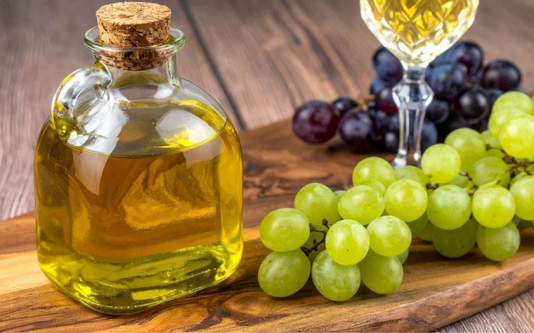 Chai dầu hạt nho vàng óng đặt cạnh chùm nho xanh và nho tím trên thớt gỗ, minh họa sự khác nhau giữa dầu hạt nho và chiết xuất hạt nho