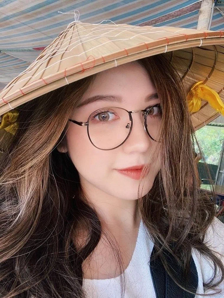 An Japan tóc nền nâu có sợi highlight sáng màu, dài quá ngực, uốn sóng lơi, đội nón lá, đeo kính gọng tròn