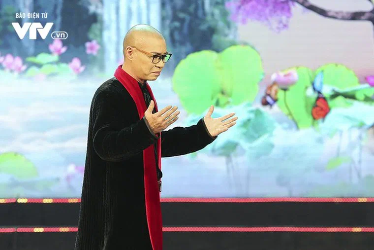 Công Lý trong vai Bắc Đẩu năm 2019, đầu cạo trọc, đeo kính gọng nâu, khoác áo nhung đen, quàng khăn đỏ