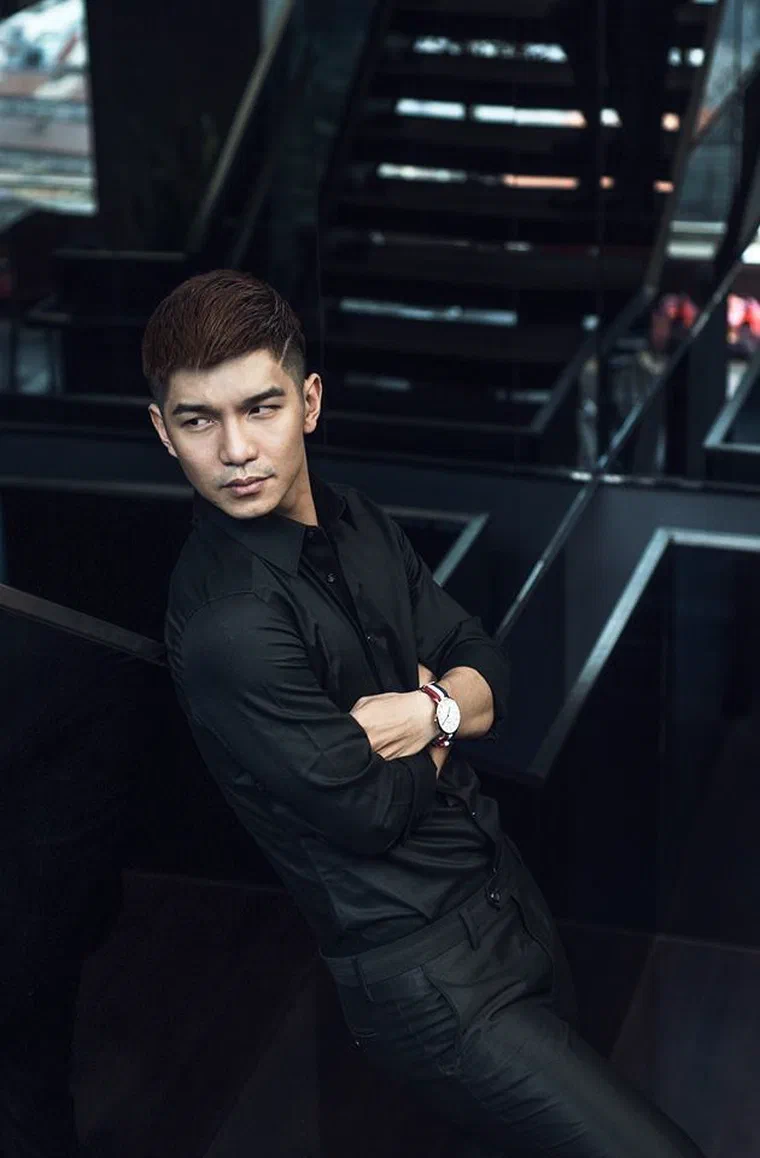 Cường Seven mặc áo đen, tóc nhuộm nâu chải lệch sang một bên, hai bên tỉa mỏng dần
