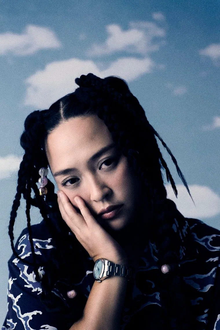Kimmese với tóc tết braids đen, rẽ ngôi giữa, phần đỉnh vấn thành một búi nhỏ, vài hạt trong suốt gắn ở bím trước thái dương