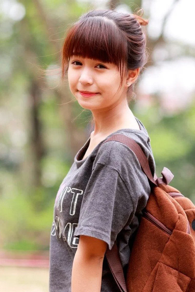 Mẫn Tiên tóc nâu ánh đỏ búi cao trên đỉnh đầu, mái bằng dày tỉa nhẹ ngang lông mày, đeo ba lô, chụp ngoài trời
