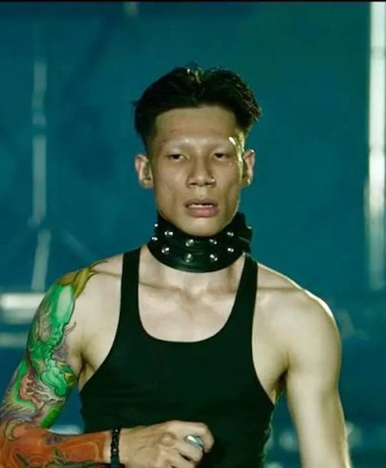 MCK trên sân khấu, tóc để tối cắt cao hai bên thành đường sắc trên vành tai, đỉnh ngắn hất ngược, lông mày cạo sạch, đeo vòng cổ đinh tán