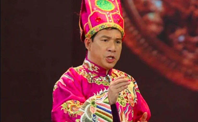 Quang Thắng trong vai Táo Kinh tế, áo bào hồng thêu, đội mũ Táo hồng đính đá đỏ, chỉ lộ tóc mai đen cắt ngắn