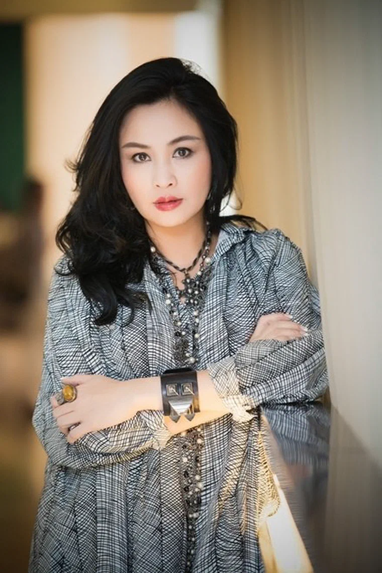 Thanh Lam với tóc đen dài qua vai, rẽ ngôi lệch, một bên vén sau tai, bên kia buông lọn sóng lớn trước vai