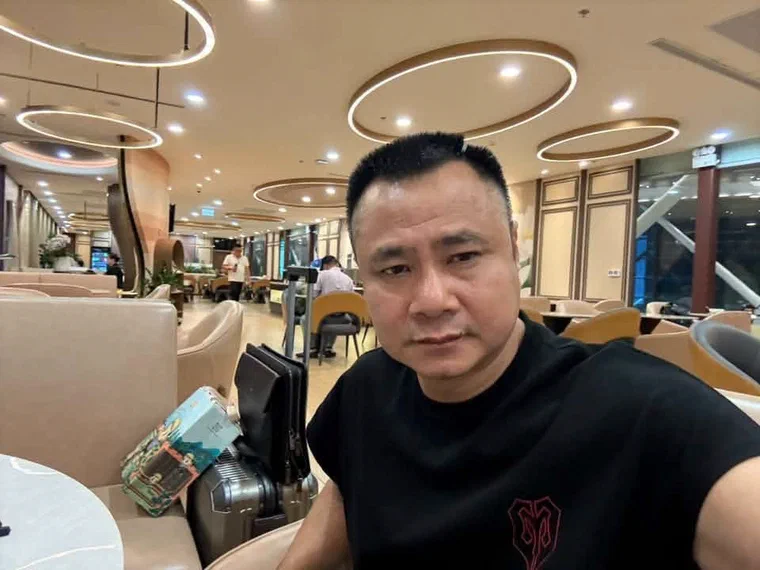 Tự Long mặc áo thun đen, tự chụp ở phòng chờ sân bay, tóc đen ngắn, phần đỉnh đã dài ra, dựng tự nhiên và hơi rối