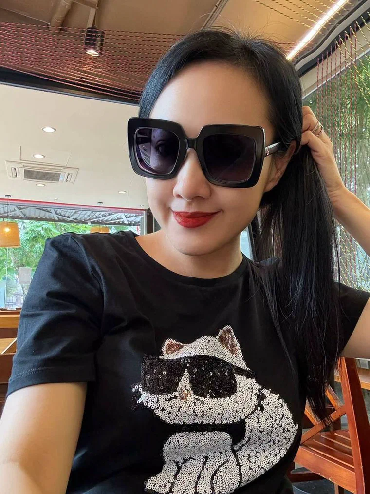 Vân Dung đeo kính râm gọng vuông, áo phông đen, tóc đen dài vuốt ngược không mái, một tay giữ đuôi tóc buộc phía sau